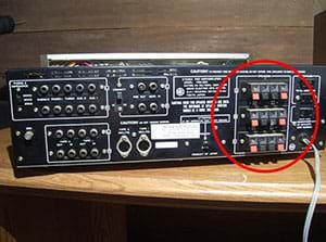 A photograph shows an amplifier with a front panel composed of ~40 various types of plugs and switches. The portion of the panel containing 12 red and black spring-loaded terminals is circled in red.