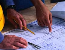 Photo shows hands, pencil and compass on a laid-out blueprint drawings.