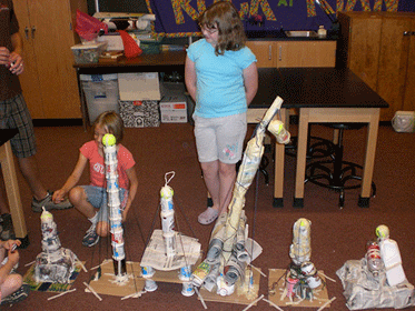 Photo shows two students behind a row of six towers.