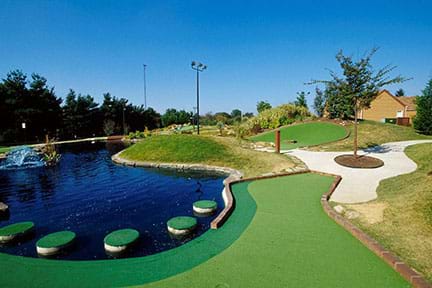 A photograph shows a pond on the left with a mini putting green to the right. Part of the green is edged with bricks to keep golf balls from rolling into the water.
