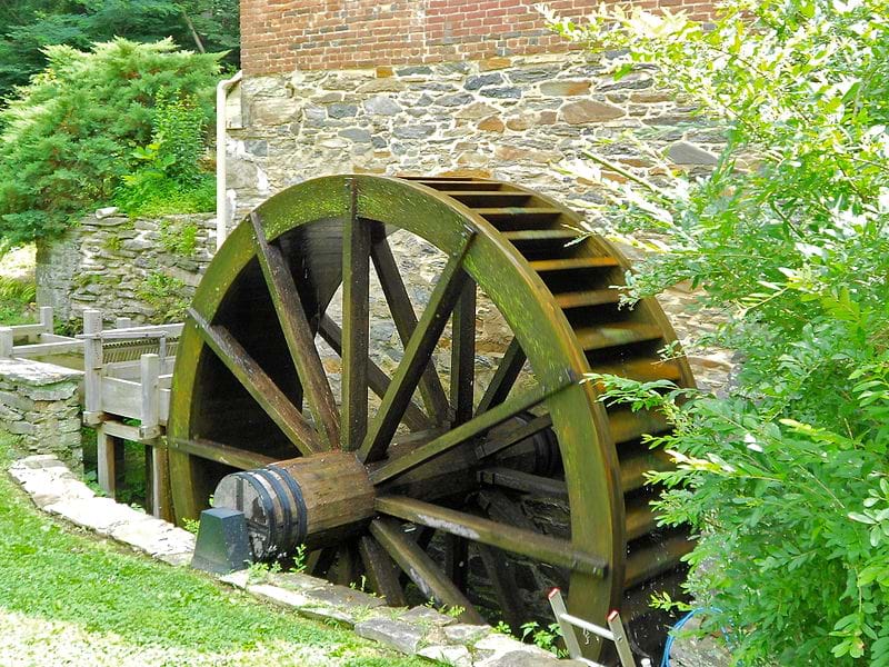 A photograph shows a large wooden water wheel near a stone structure and creek.