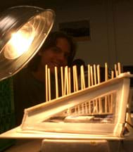 Photo shows a large light bulb in a lamp, shining on a shoe box-sized model home with a foam-core board shed roof and big side windows, and a cabled temperature sensor inside.