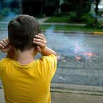 A photograph shows a little boy covering his ears after firecrackers make loud bangs in the streets.