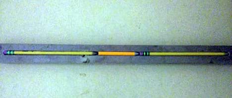A photograph shows three pencils, lined up in a piece of wood with a groove cut down the middle of it, as a tray.