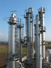 Photo shows five tall silver towers clustered together with curving pipes coming out of the tops and ladders running up each tower.