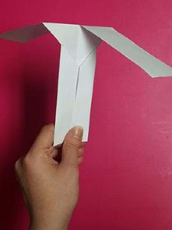 A hand holds a simple “helicopter” made from cut and folded paper.
