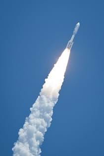 The launch of the Juno rocket heading off into the blue sky at an angle, with puffs of white exhaust trailing behind.