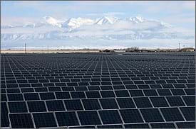 Photo shows thousands of dark blue gridded panels as far as the eye can see with a blue sky and mountains in the distance.