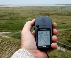 A photograph shows a man's hand holding a Garmin rand GPS receiver, which looks like a plastic remote control device with buttons and a display screen.