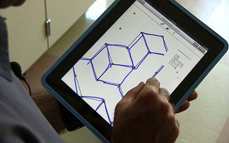 A photograph shows a hand sketching an isometric drawing of an object on a handheld tablet computer.