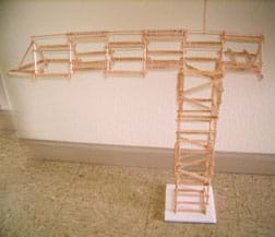 About 100 Popsicle sticks glued end-to-end to create a truss-like tower with a horizontal top structure longer on one side than the other.