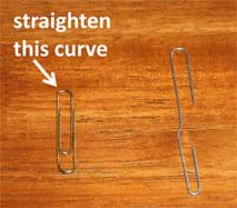 Photo shows two shiny wire paper clips on a table top. An arrow points to the top curve of one paper clip with a message: straighten this curve. The other paper clip has been opened up (the curve straightened) so that each end of the wire has a hook. 