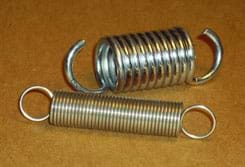 Photo shows two tension springs: a short and wide one made of thick metal and a longer, thinner one made of much thinner metal.