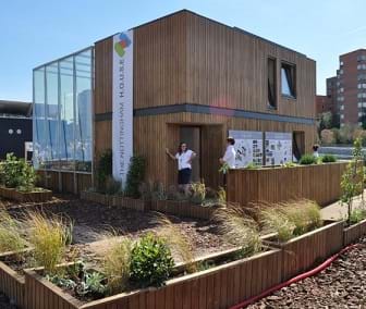 A photograph shows the Nottingham HOUSE (home optimising the use of solar energy) built as part of the Solar Decathlon 2010 event--a cube-shaped structure.