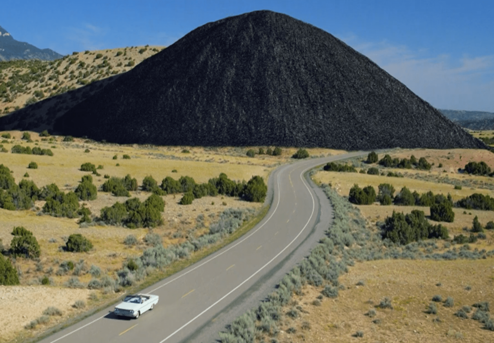 A screenshot from a video showing a car driving past a large pile of carbon. 