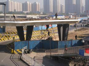 Construction workers building a new highway overpass. Tall apartment buildings are in the background.