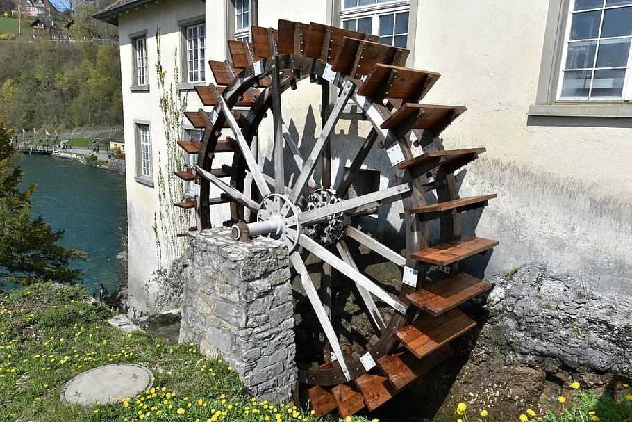 An image of a waterwheel mill by a white house and river.