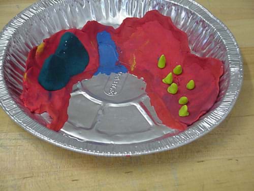 A photograph shows an aluminum pie tin with red, blue and green clay shapes in the bottom.