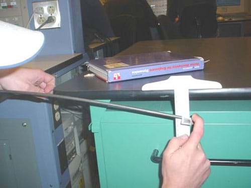 A photograph shows a student using a meter stick to measure the deflection of an aluminum rod after applying a force to one end.