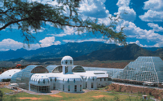 Photo of glass domes and greenhouses with a mountain backdrop.