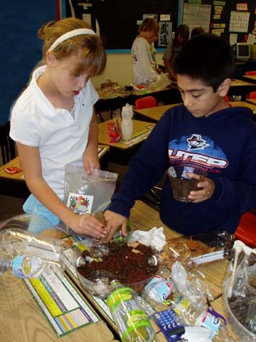 Two students place soil in their plastic biodome base.