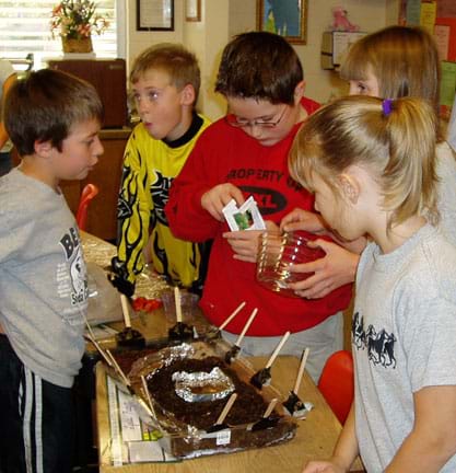 Five students cluster around their model biodome as one plants seeds in the soil.