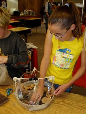 Photo of a girl putting material into the bottom of her plastic model biodome.