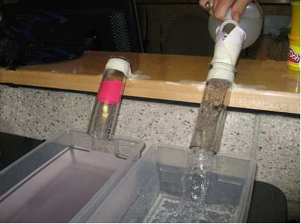 Photo shows two clear tubes, each positioned at 45° angles above separate plastic containers. Water pours through the unclogged "artery" into the bin.