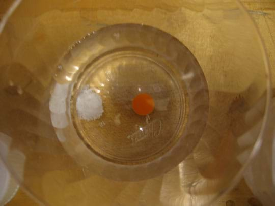 Photo view from above a clear glass shows a red tablet in clear liquid.