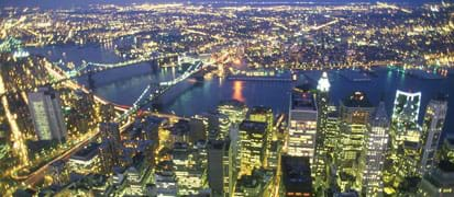 Evening aerial photo shows twinkling skyscraper and bridge lights.