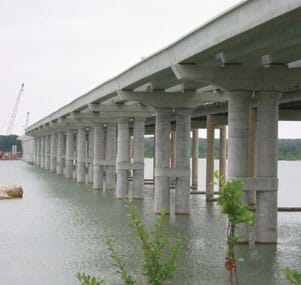 Photo shows a row of concrete columns and beams that compose a bridge crossing a body of water.