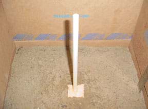 Photo shows the block of wood at the end of a dowel partially submerged in the top soil layer in a cardboard box.