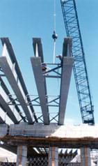 Photo shows a crane moving huge steel I-beams.