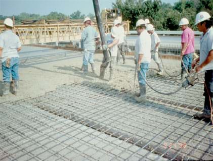 Photo shows men in construction hats and rubber boots walking on a metal grid.