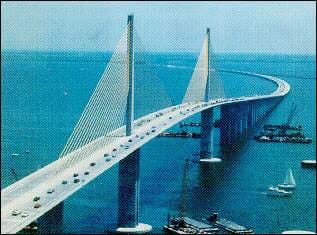 Photo shows a multi-lane bridge over water on columns, with cables attached to two support towers like the strings of a harp.