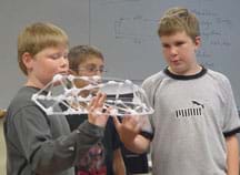 Photo of three boys holding a model bridge made of straws and tape.