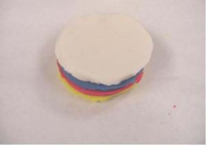 A photograph shows four circular layers of different colors of modeling clay (yellow, red, blue white) stacked on top of one another.