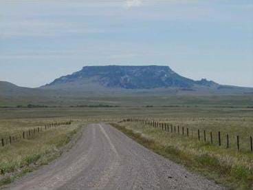 A photograph shows a dirt road leading towards a wide, flat-topped mountain in the distance.