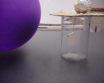A photograph shows a charged balloon positioned near the foil ball on top of a jar. Inside the glass jar, the silver foil leaves have swung toward the balloon.