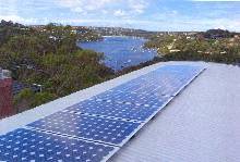 A photograph showing bright light reflecting off of a solar panel that is composed of many iridescent blue photovoltaic cells connected together in rectangular panels. 