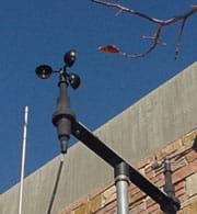 Photograph of a black, three-cup anemometer attached to a pole.