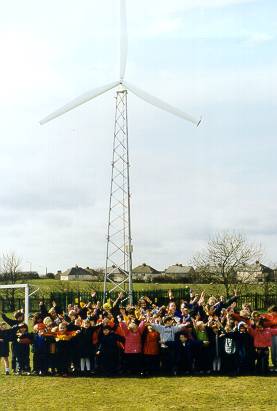 A photograph shows large group of school children standing in front of a tall, three-blade wind turbine.