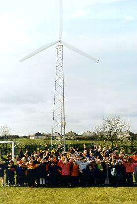 A photograph shows large group of school children standing in front of a tall, three-blade wind turbine.