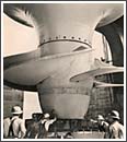 A photograph shows workers in hardhats moving a gigantic, multi-bladed turbine into place.