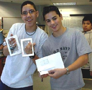 A picture of two 8th grade boys holding their pollution collectors and the graph paper they used to analyze the data.