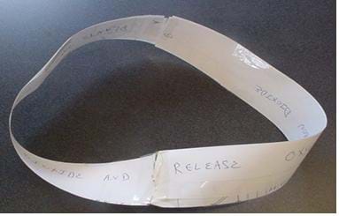 Photo shows a strip of paper, twisted and taped, so that it has become a completed circle with no beginning and no end.