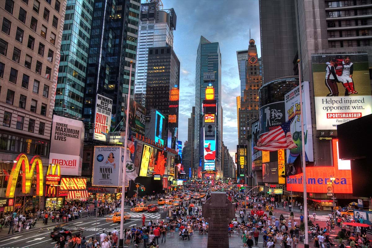 A photo of Times Square, Manhattan, New York, showing crowds of people, bright signs and advertisements, and tall buildings. 