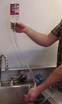 A photograph shows a cola bottle held upside down over a sink with clear plastic tubing attached with duct tape to the bottle neck. The bottle is filled with water.