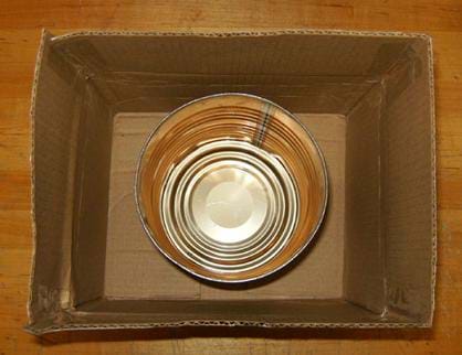 A photo looking down into a cardboard box with an open metal coffee can placed at the bottom.