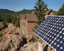 Photo shows a panel of solar cells on a rocky hillside near a home.